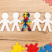 Top view of special kid with autism among another and pieces of multicolored puzzle on wooden background